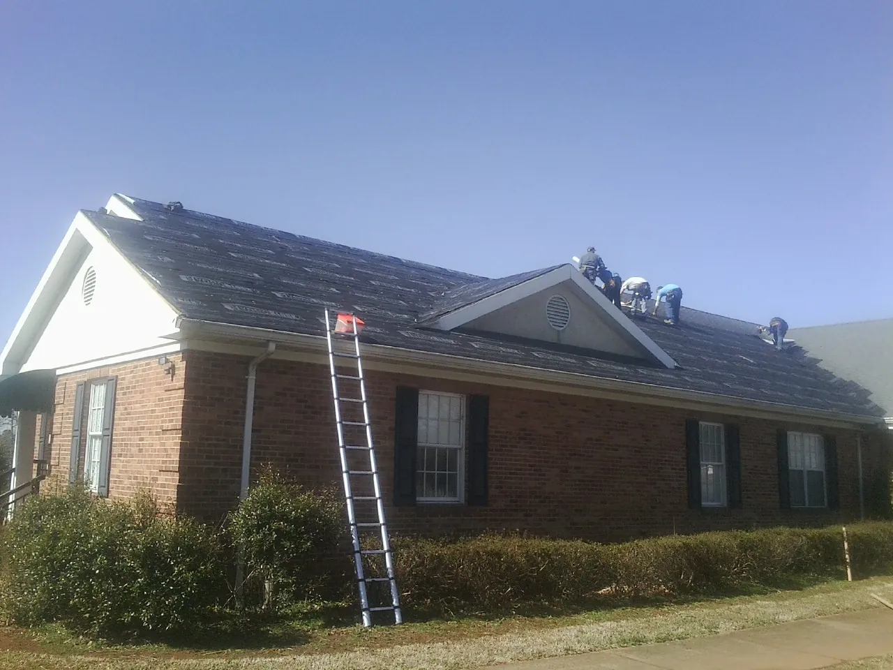 Crew tearing shingles off a brick ranch roof with a ladder set — Metal Roof Repair work by our crew in Beech Bottom