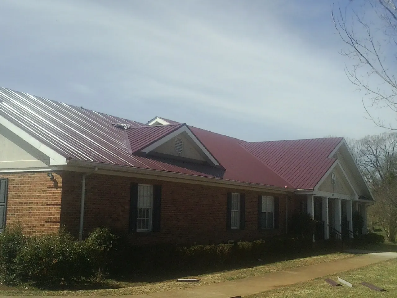 Red metal roof with gabled entries on a long brick building, from a Hail Damage Roof Repair job in Beech Bottom
