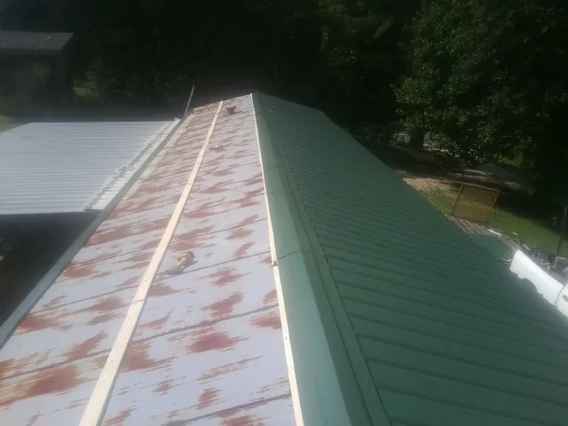 Old rusted panels beside newly installed green metal roofing — Wind Damage Roof Repair by Roofing Brothers in Beech Bottom