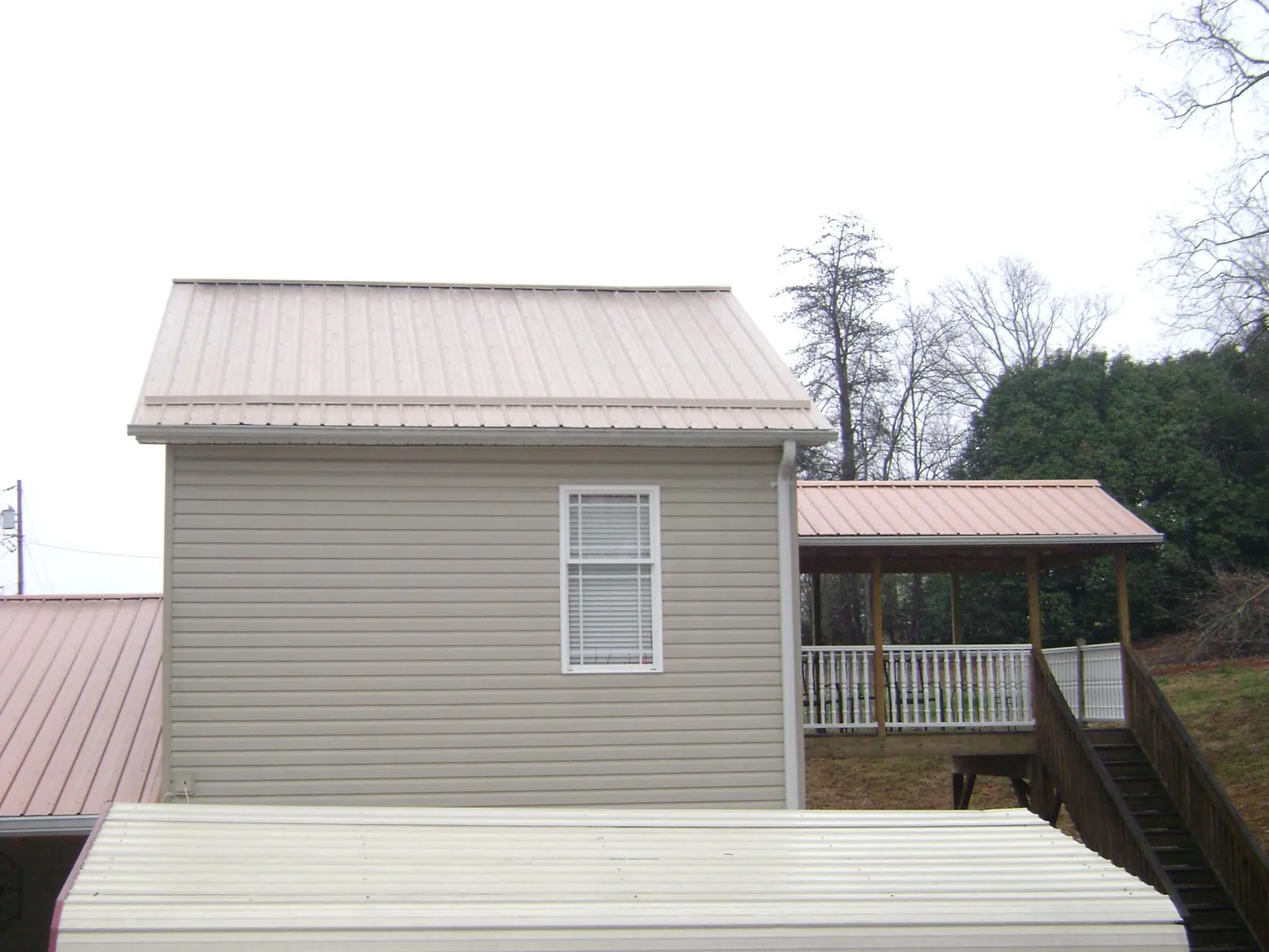 Tan metal roofs on a two story addition and attached porch, from a Roof Replacement job in Beech Bottom
